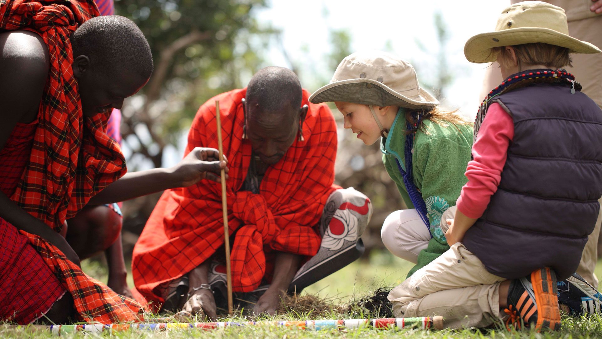 Maasai hosts sharing a traditional activity with visiting children